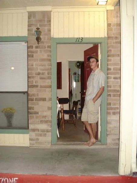 Me standing barefoot in the doorway of apartment 113, a brick building with green trim