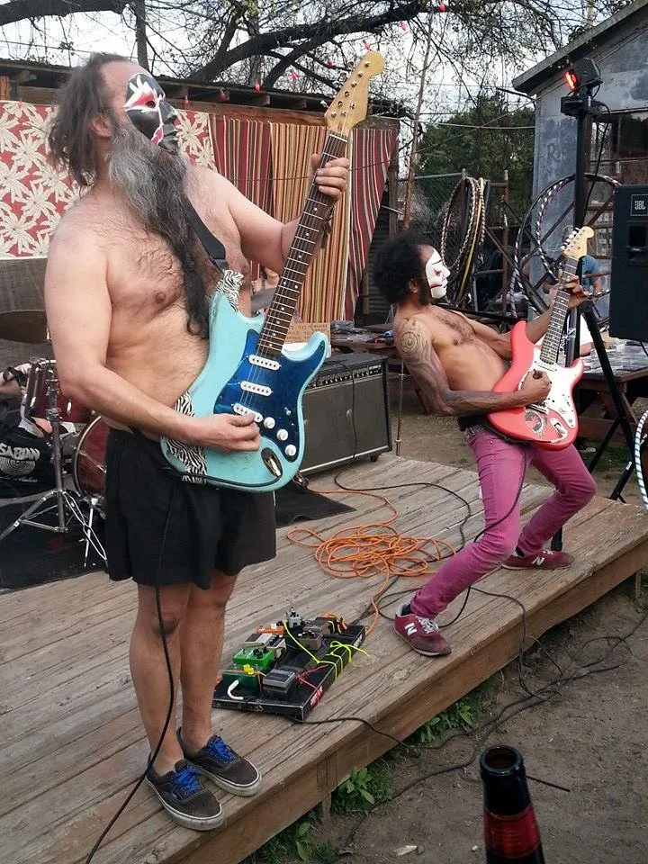 Daikaiju playing an outdoor stage in kabuki masks, shirtless, guitars slung high