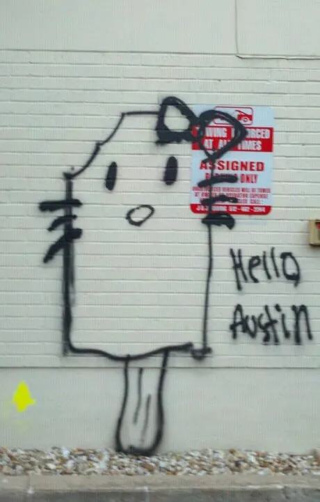 Hello Kitty spray-painted on a cream brick wall beside a parking sign, with “Hello Austin” written next to it in the same hand