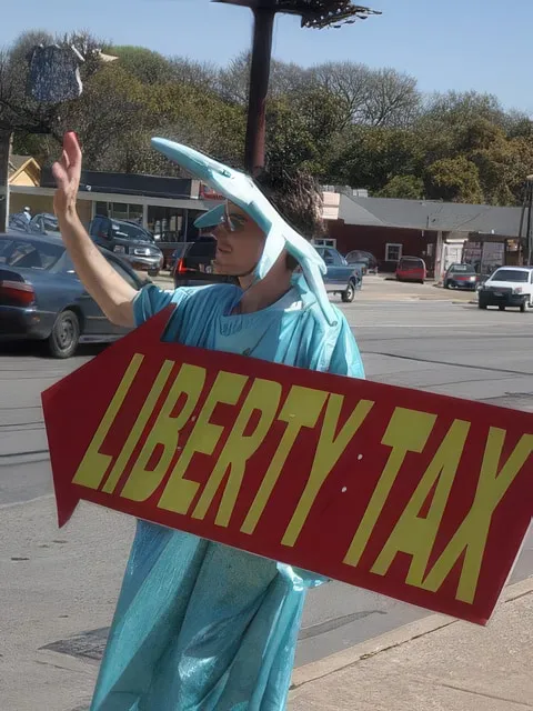Me on a roadside in a Statue of Liberty costume and foam crown, holding a large red arrow sign reading LIBERTY TAX