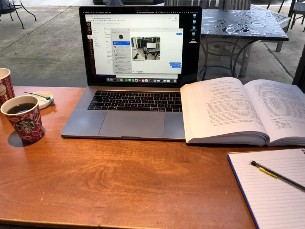 A laptop, an open textbook, a legal pad and a Starbucks cup on a cafe table