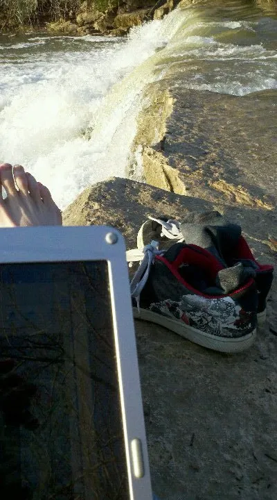 A laptop, shoes and bare feet on the rock ledge beside the falls at Twin Falls